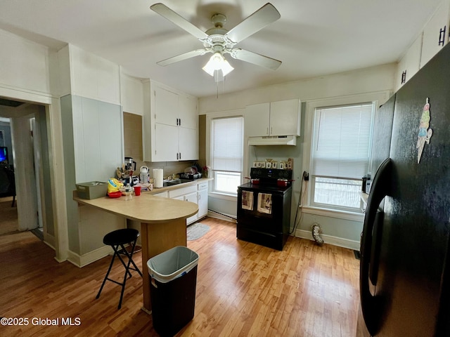 kitchen with black appliances, a peninsula, under cabinet range hood, and light wood-type flooring
