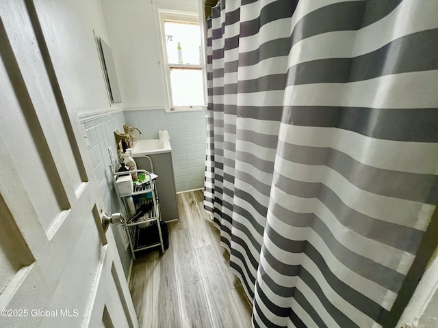 bathroom with wood finished floors, wainscoting, vanity, tile walls, and a shower with shower curtain