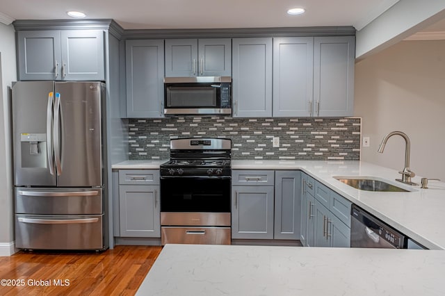 kitchen featuring appliances with stainless steel finishes, a sink, gray cabinetry, light wood finished floors, and tasteful backsplash
