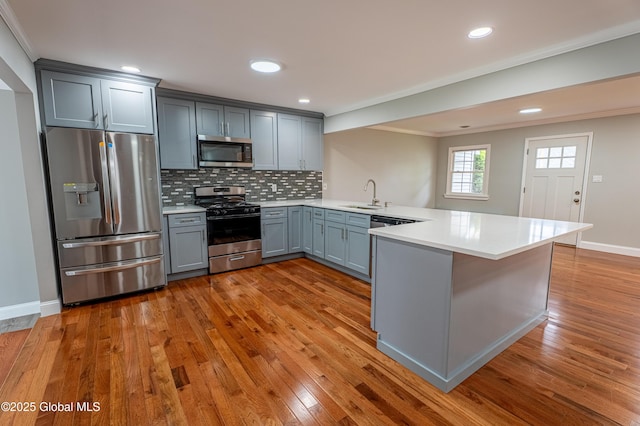 kitchen with appliances with stainless steel finishes, a sink, a peninsula, gray cabinets, and hardwood / wood-style flooring
