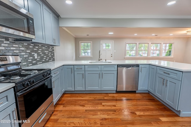 kitchen with appliances with stainless steel finishes, a sink, ornamental molding, light countertops, and a peninsula