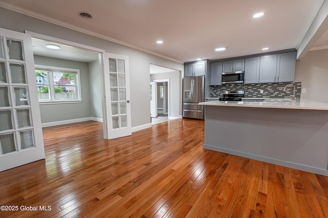 kitchen with stainless steel appliances, gray cabinetry, ornamental molding, light countertops, and a peninsula
