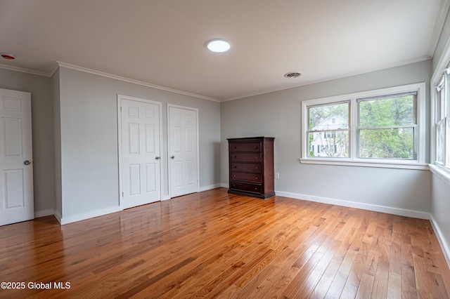 unfurnished bedroom featuring light wood-style floors, crown molding, baseboards, and a closet