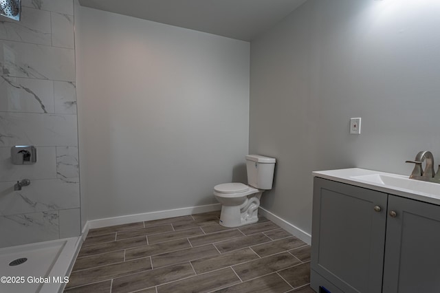 bathroom with tiled shower, baseboards, toilet, wood tiled floors, and vanity