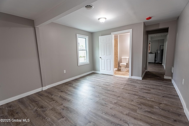 unfurnished bedroom with wood finished floors, baseboards, washer / dryer, and ensuite bathroom