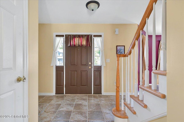 foyer entrance with stairs, baseboards, and stone finish floors