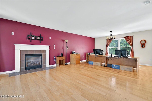 unfurnished office with wood finished floors, a chandelier, a tile fireplace, and baseboards