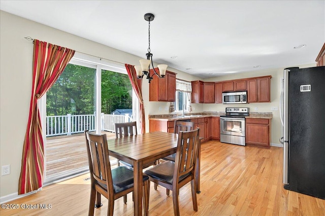 dining area with light wood-style floors, healthy amount of natural light, baseboards, and a chandelier