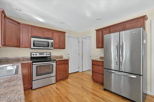 kitchen with stainless steel appliances, light wood finished floors, a sink, recessed lighting, and brown cabinets