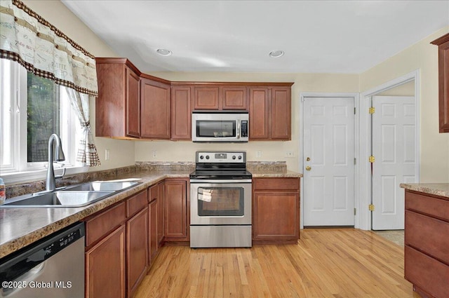 kitchen with stainless steel appliances, a sink, light wood-type flooring, brown cabinets, and recessed lighting
