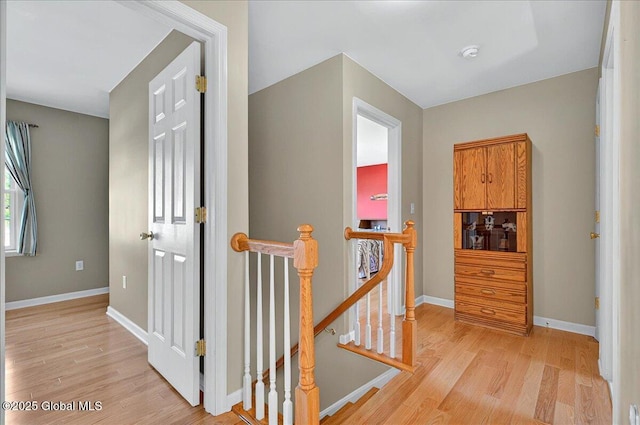 hall with an upstairs landing, light wood finished floors, and baseboards
