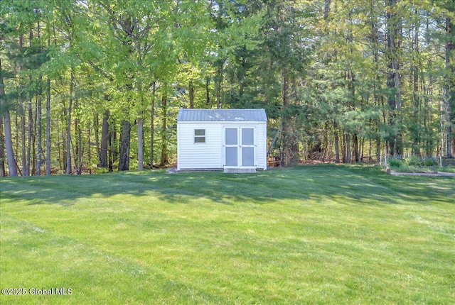 view of grassy yard with a storage shed, an outbuilding, and a wooded view