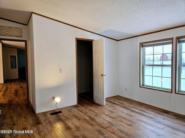 unfurnished bedroom featuring ornamental molding, wood finished floors, a textured ceiling, and a closet