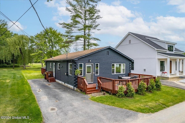 view of front of house with driveway, log siding, a front lawn, a deck, and roof with shingles