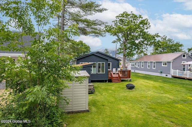 rear view of property with a wooden deck, a yard, a storage shed, and an outbuilding