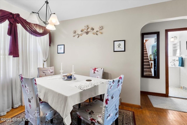 dining room featuring wood-type flooring, arched walkways, baseboards, a chandelier, and stairs