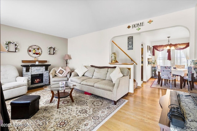 living room featuring a chandelier, light wood-type flooring, a stone fireplace, stairway, and baseboards