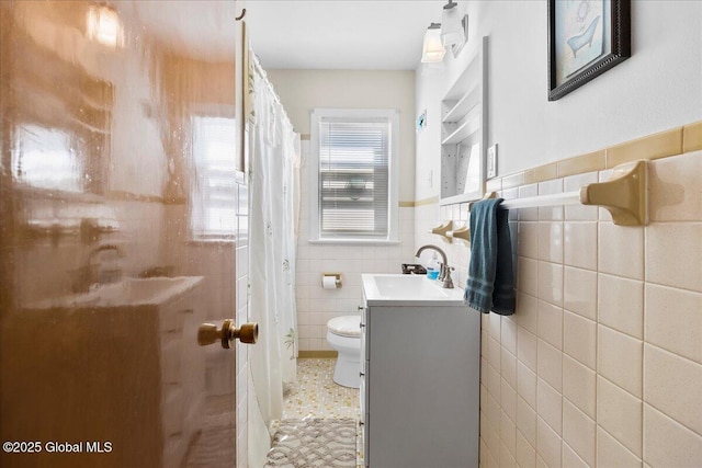 bathroom with tile walls, toilet, vanity, curtained shower, and a wainscoted wall