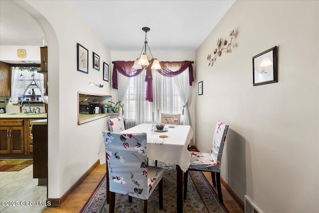 dining area with arched walkways, light wood-style floors, and baseboards