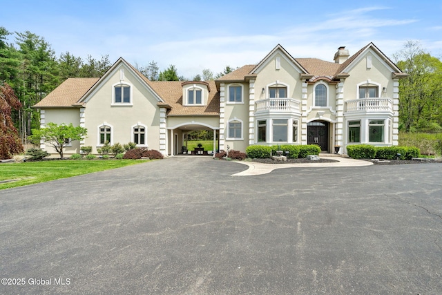 view of front of property featuring a chimney, a balcony, stucco siding, and roof with shingles