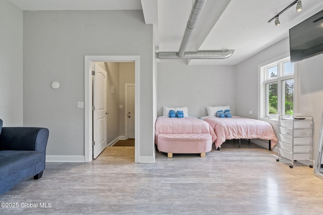 bedroom with wood finished floors, baseboards, and rail lighting