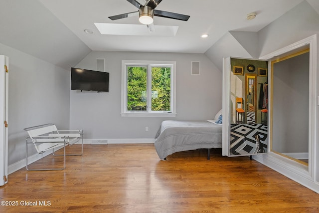 bedroom with a skylight, lofted ceiling, wood finished floors, baseboards, and a ceiling fan