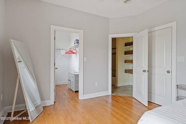 unfurnished bedroom with a spacious closet, light wood-style flooring, a closet, and baseboards
