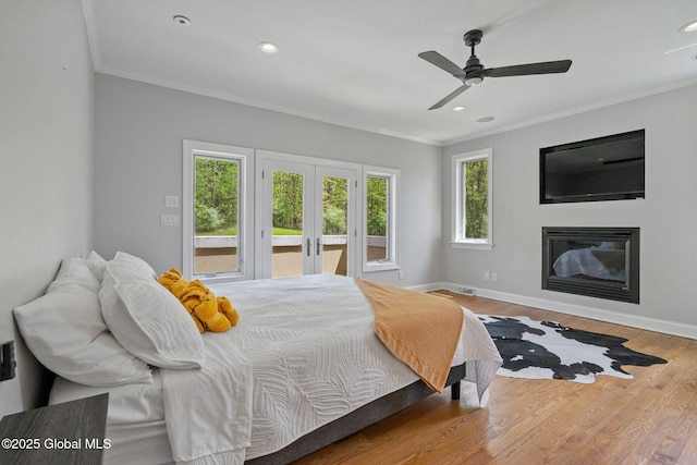bedroom featuring crown molding, french doors, wood finished floors, access to exterior, and a glass covered fireplace