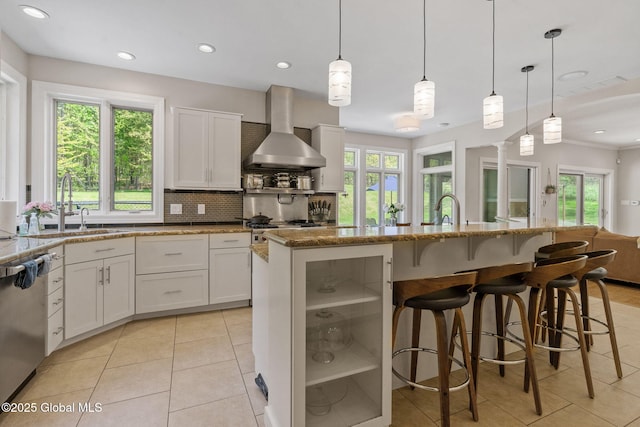 kitchen with wall chimney range hood, a sink, light tile patterned floors, plenty of natural light, and recessed lighting