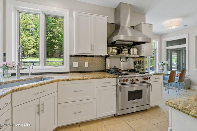 kitchen featuring luxury range, wall chimney range hood, a sink, light stone counters, and light tile patterned floors