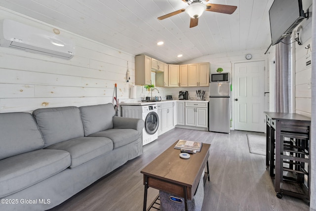 living area featuring an AC wall unit, wood finished floors, washer / dryer, lofted ceiling, and a ceiling fan