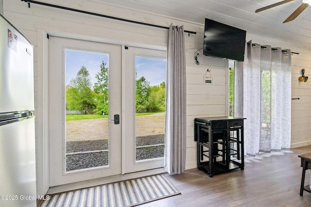 doorway with ceiling fan, wood walls, and wood finished floors