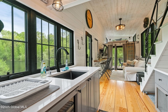 kitchen featuring a sink, light wood finished floors, light countertops, pendant lighting, and wooden ceiling