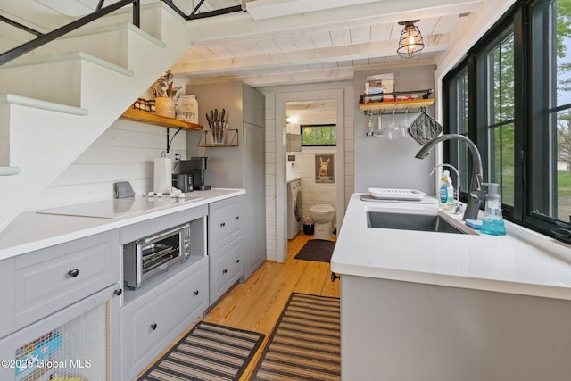 kitchen with open shelves, a sink, washer / clothes dryer, light wood-style floors, and electric cooktop