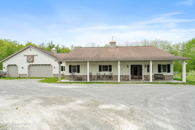 view of front of house featuring stone siding, a porch, dirt driveway, and roof with shingles