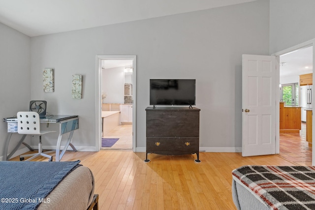bedroom with baseboards, wood finished floors, white fridge, and ensuite bath