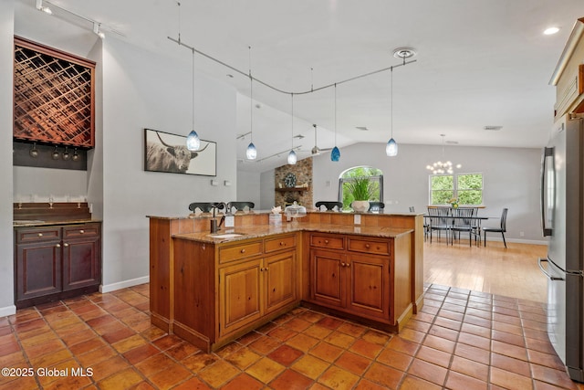 kitchen with freestanding refrigerator, vaulted ceiling, baseboards, hanging light fixtures, and light stone counters