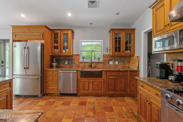 kitchen featuring stainless steel appliances, a sink, wall chimney range hood, brown cabinetry, and recessed lighting