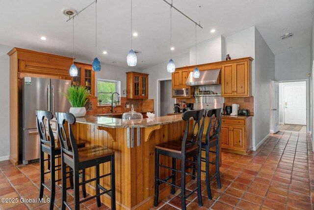 kitchen featuring stainless steel appliances, decorative backsplash, glass insert cabinets, light stone countertops, and range hood