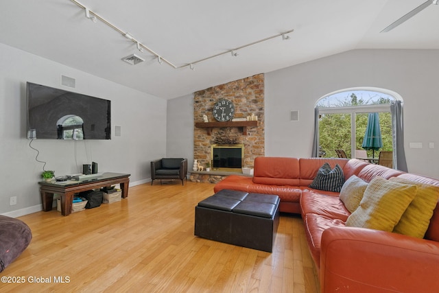 living room with track lighting, vaulted ceiling, light wood-type flooring, baseboards, and a stone fireplace