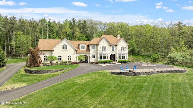 french country style house featuring a balcony, a chimney, a front lawn, and stucco siding