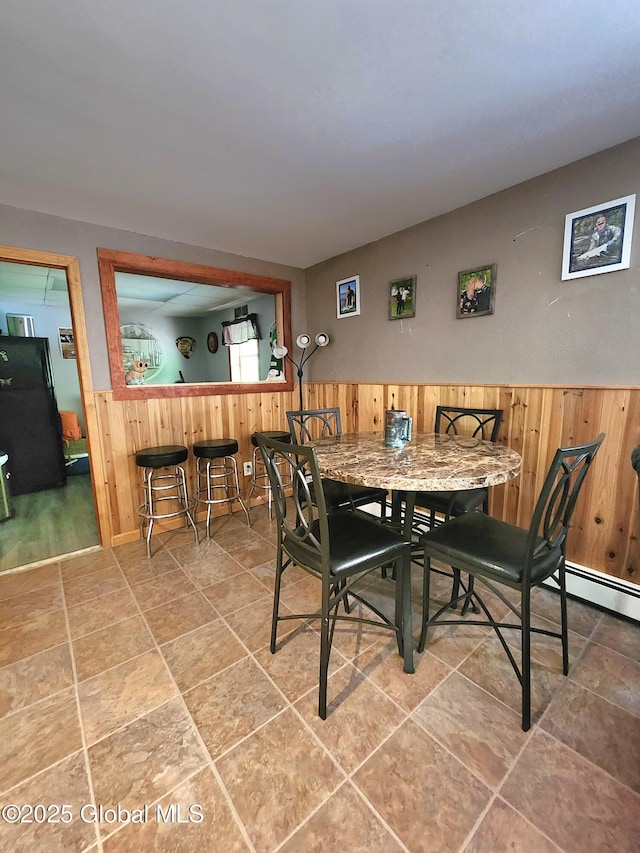dining room featuring wooden walls, a wainscoted wall, bar area, and a baseboard radiator