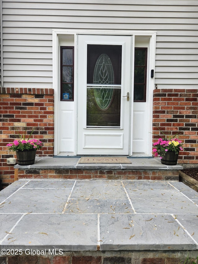view of exterior entry with uncovered parking and brick siding