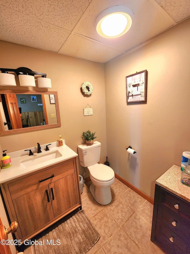 bathroom with toilet, a drop ceiling, vanity, tile patterned flooring, and baseboards