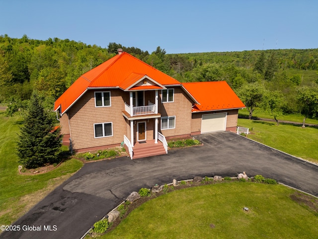 1435 Webster St, Malone, NY 12953 - view of front of property featuring a balcony, a wooded view, asphalt driveway, a garage, and a front lawn
