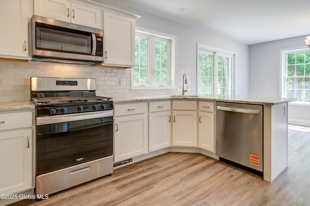 kitchen with stainless steel appliances, a sink, light wood-style flooring, tasteful backsplash, and white cabinets