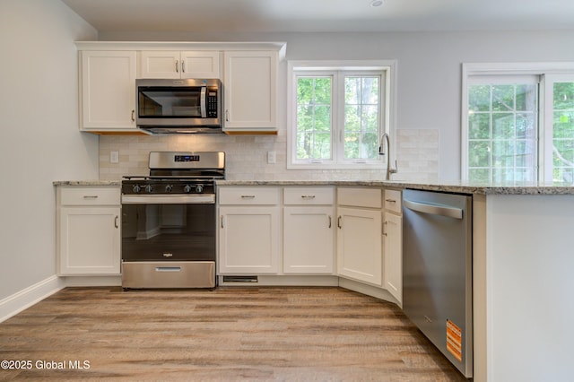 kitchen with appliances with stainless steel finishes, light wood finished floors, a sink, white cabinetry, and plenty of natural light
