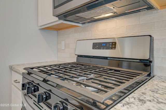 kitchen view of stainless steel range with gas stovetop, white cabinetry, tasteful backsplash, and light stone counters
