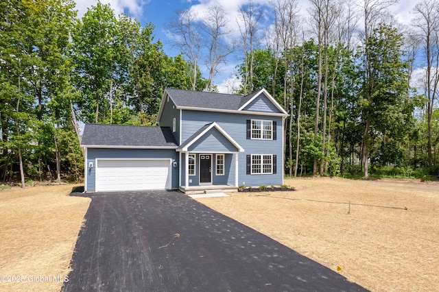 traditional home featuring driveway, an attached garage, a shingled roof, and view of wooded area