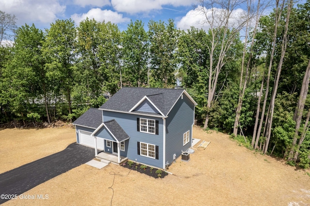 traditional-style home featuring a shingled roof, a garage, view of wooded area, and central AC unit